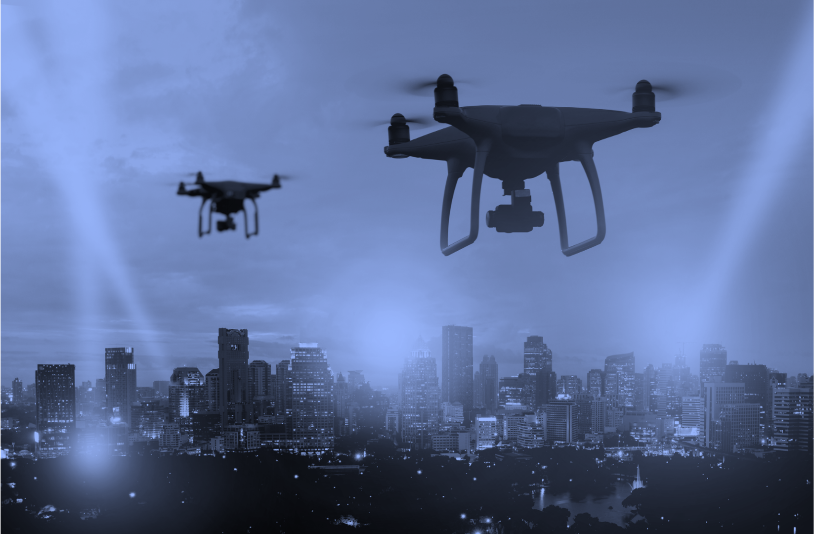 Two drones flying over a city with buildings in the background.